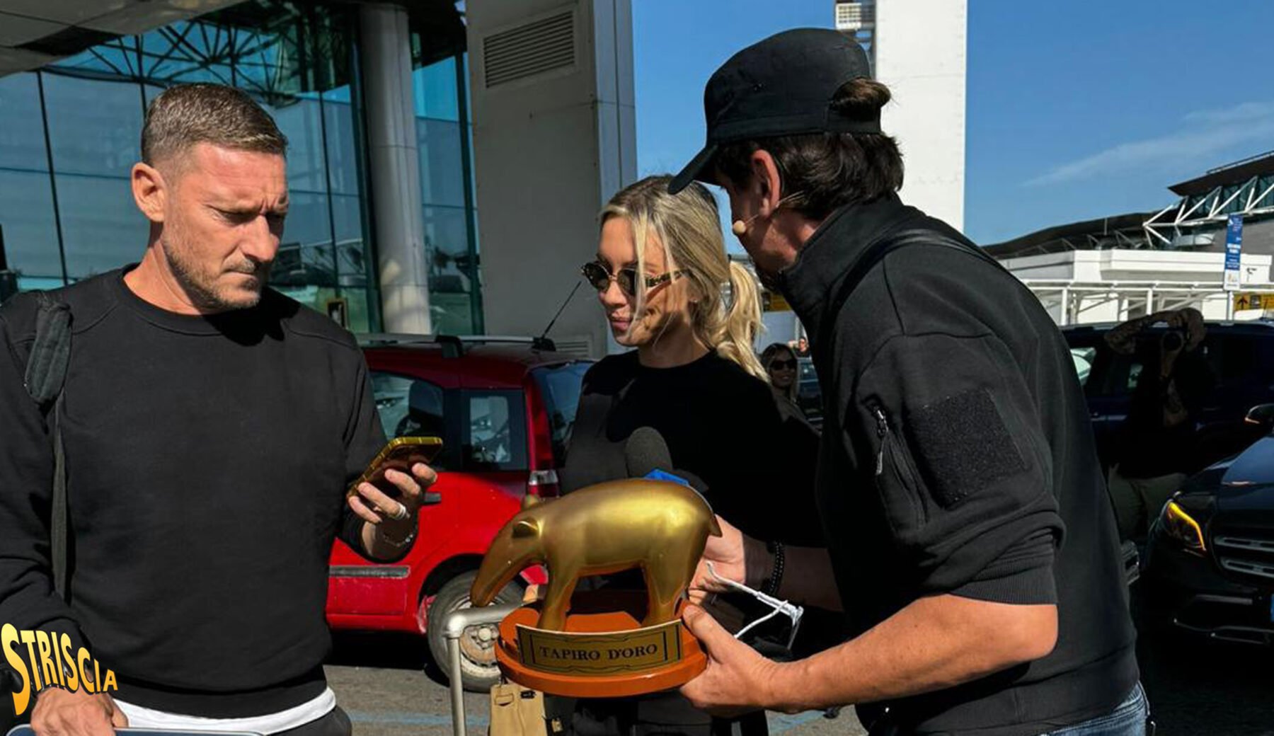 Dopo una breve fuga a Miami per un torneo di padel, Francesco Totti è tornato a Roma, accolto all’aeroporto di Fiumicino dall’inviato di Striscia la Notizia, Valerio Staffelli, pronto a consegnargli l’ennesimo Tapiro d’Oro.